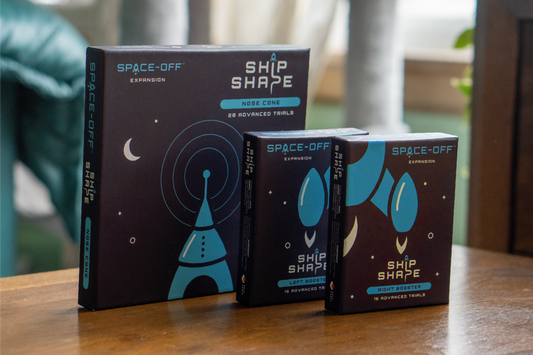 Three 'Space-Off' expansion boxes for a board game on a wooden surface.
